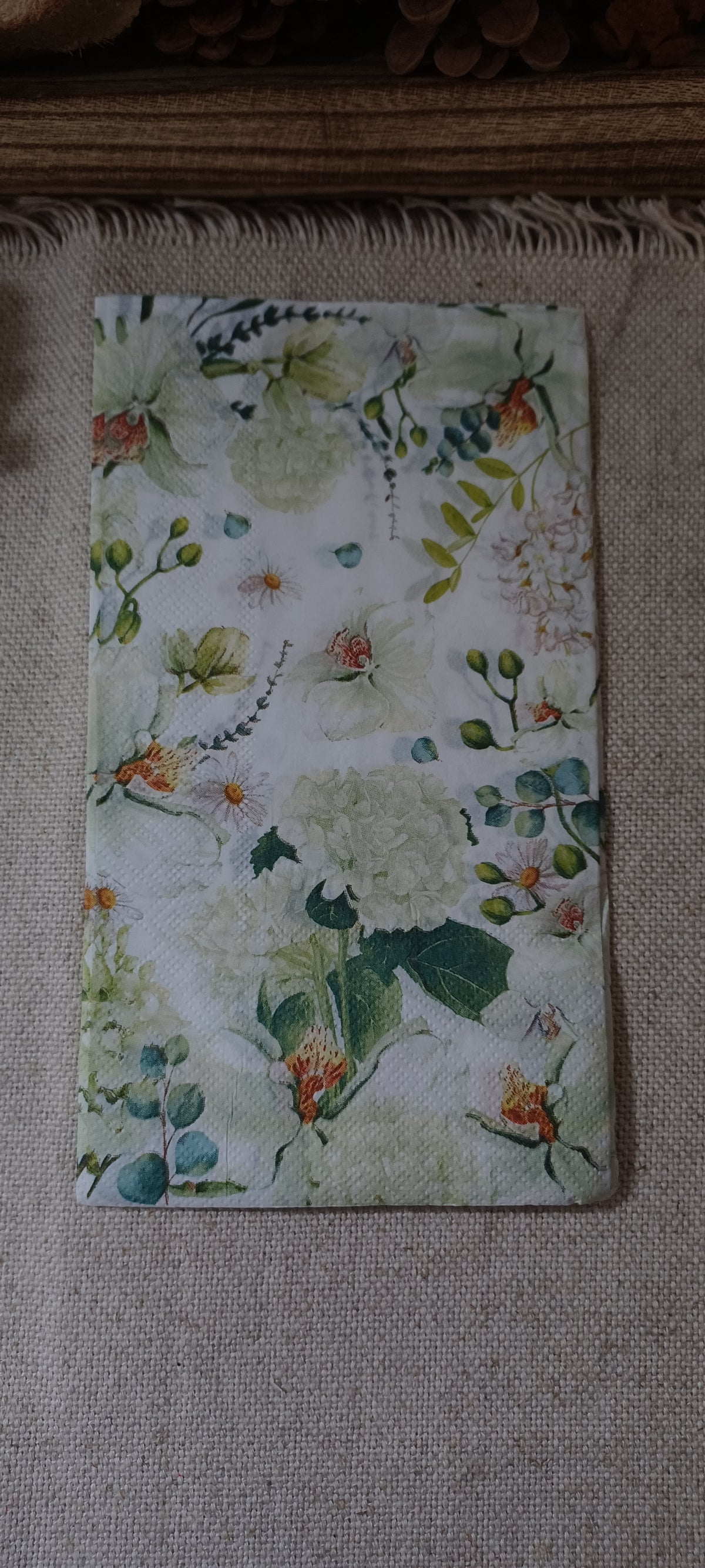 Soft watercolor botanical paper guest napkin with pale green and white flowers, daisies, rosebuds, and blue-green leafy stems.