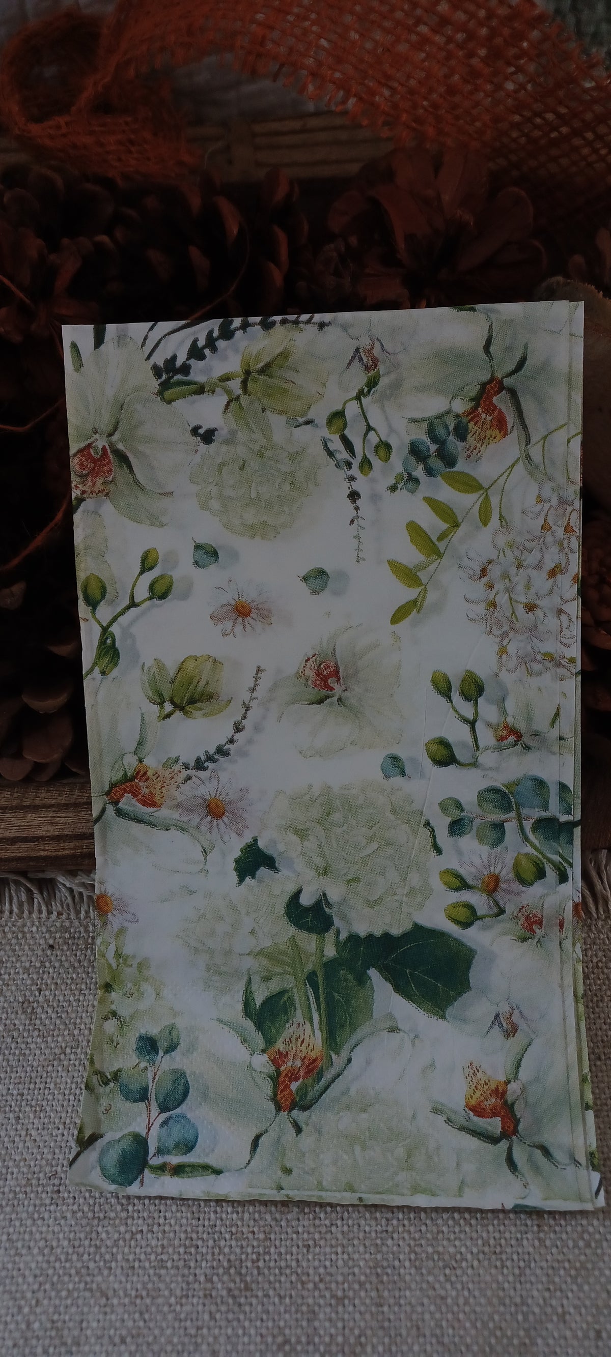 Close view of a pale botanical guest napkin featuring watercolor-style hydrangea blossoms, small flowers, buds, and foliage.