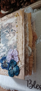 Side view of handmade cat junk journal showing its full layered pages, lace trims and ruffled edges.