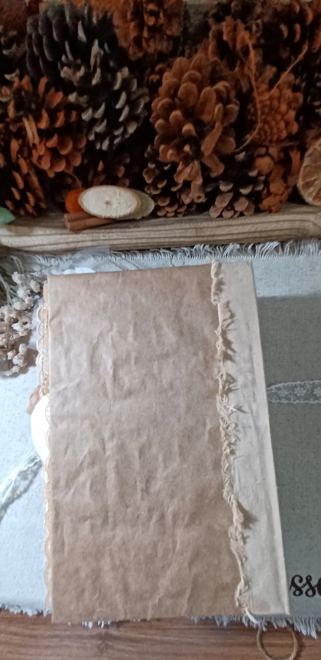 A  journal cover made with amazon packaging with a raw, frayed edge, displayed on a wooden surface with pinecones and dried botanicals in the background.