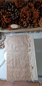 A  journal cover made with amazon packaging with a raw, frayed edge, displayed on a wooden surface with pinecones and dried botanicals in the background.