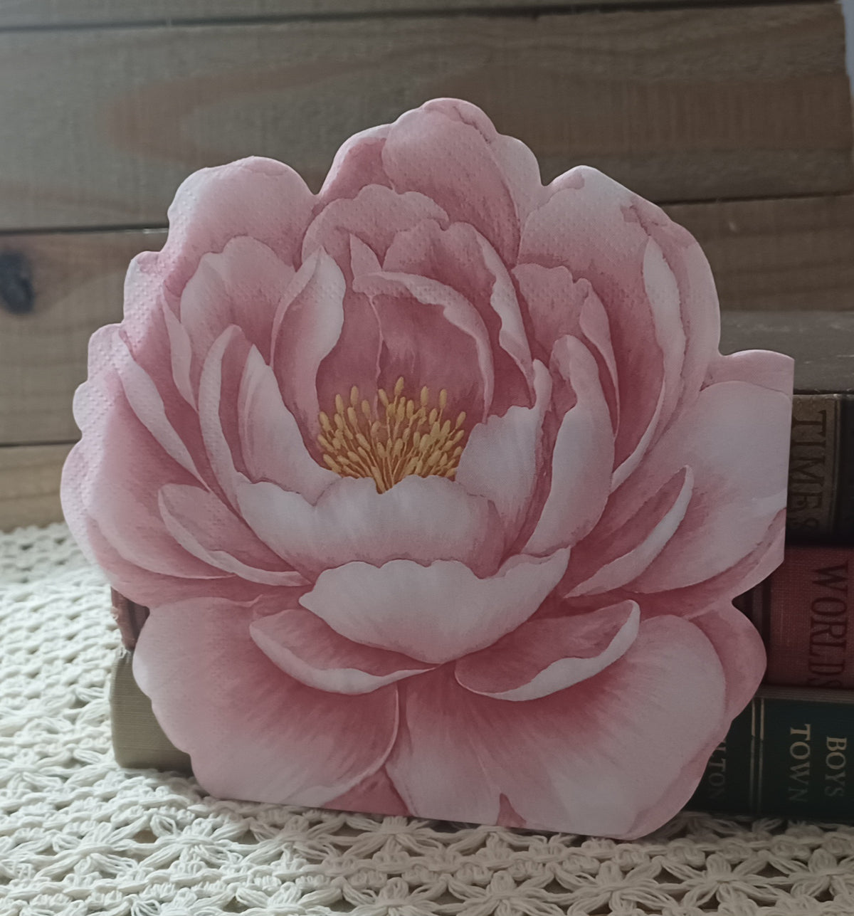 Blush pink die-cut flower paper napkin displayed upright with vintage books for scale and styling.