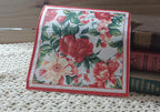 Vintage-style red and coral floral luncheon napkin displayed with old books and crochet lace.