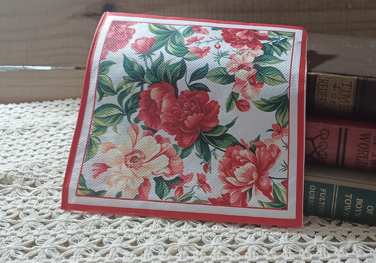 Vintage-style red and coral floral luncheon napkin displayed with old books and crochet lace.