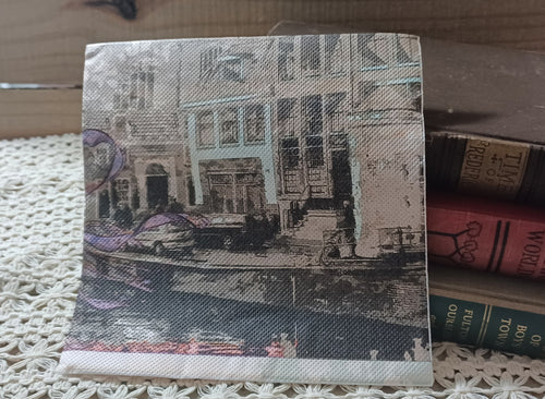 Vintage-style European canal scene luncheon napkin with faded buildings, water, and muted sepia tones.