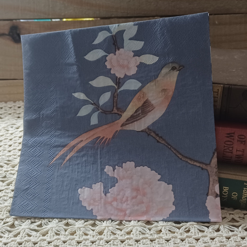 Dusty blue luncheon paper napkin featuring a blush pink and cream bird perched on a flowering branch with soft pink blossoms.