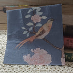 Dusty blue luncheon paper napkin featuring a blush pink and cream bird perched on a flowering branch with soft pink blossoms.