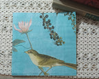 Turquoise blue bird and botanical paper napkin displayed upright beside vintage books on a crocheted textile.
