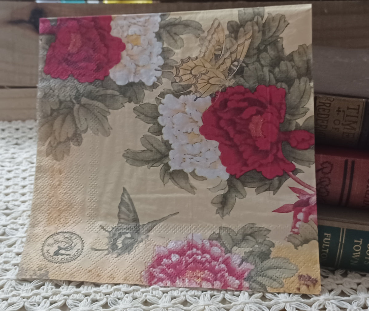 Vintage-style luncheon paper napkin with deep rose and white flowers, leafy botanicals and butterflies on a warm parchment background.