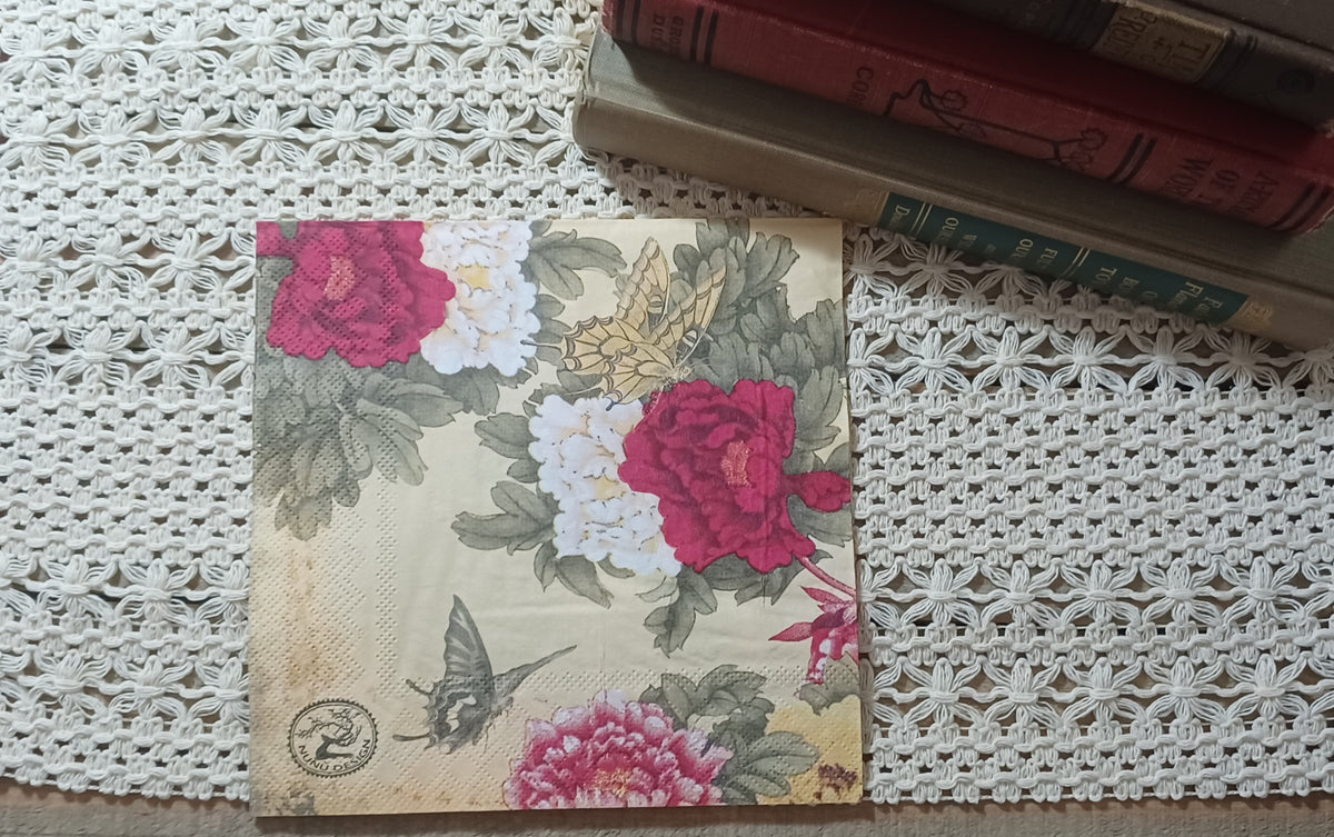 Butterfly and vintage floral paper napkin displayed upright beside old books on a cream crocheted textile.