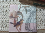 Blush pink vintage-style paper luncheon napkin featuring a small songbird, faded flower, antique handwriting and architectural illustration.