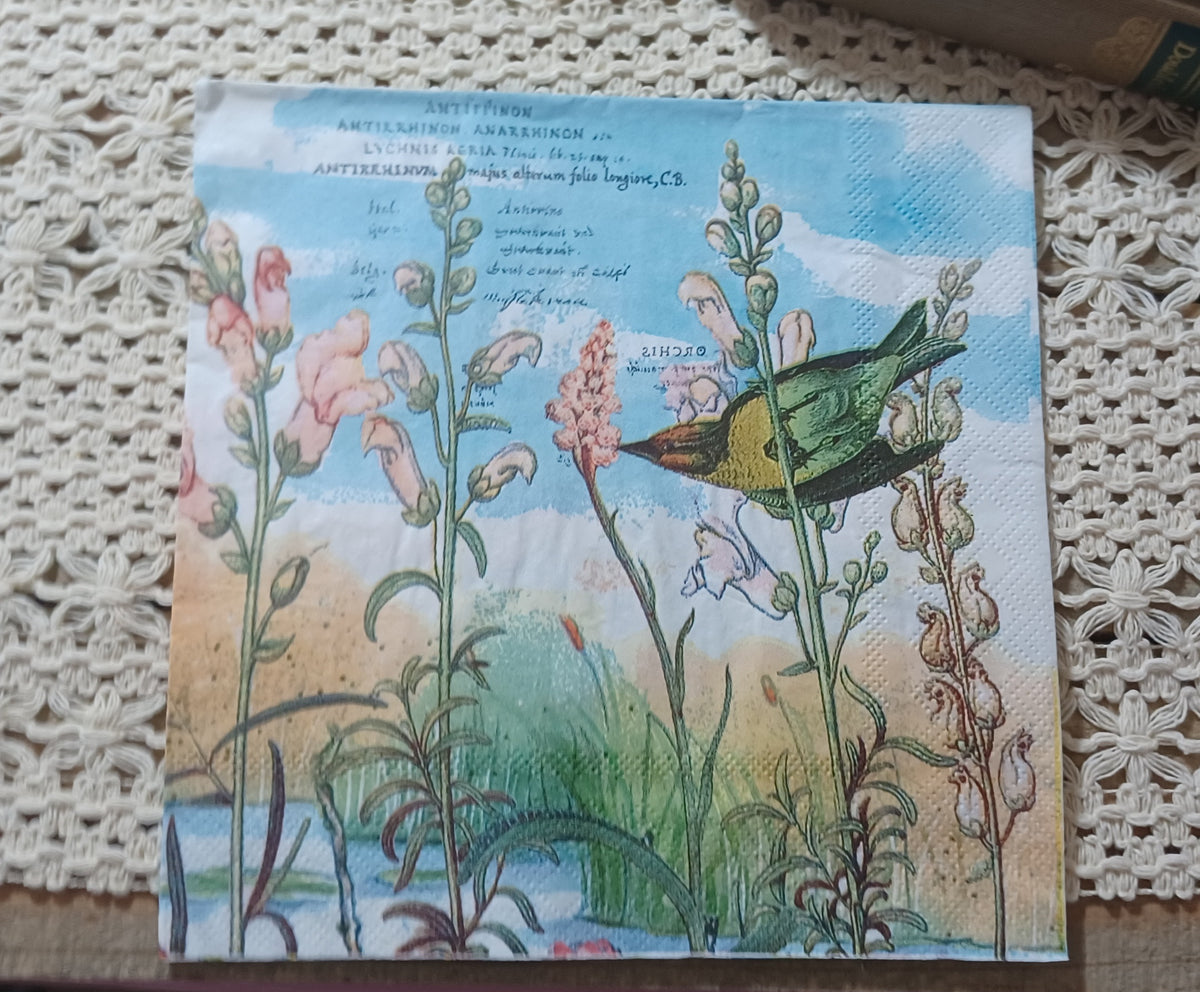 Decorative paper napkin with a vintage green and yellow bird, pink wildflowers, botanical stems, and faded script against a pale blue sky.