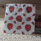 Individual decorative paper napkin with a repeating pattern of red and black watercolor-style ladybugs on a pale background.