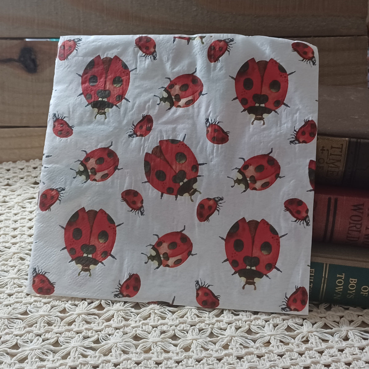 Individual decorative paper napkin with a repeating pattern of red and black watercolor-style ladybugs on a pale background.