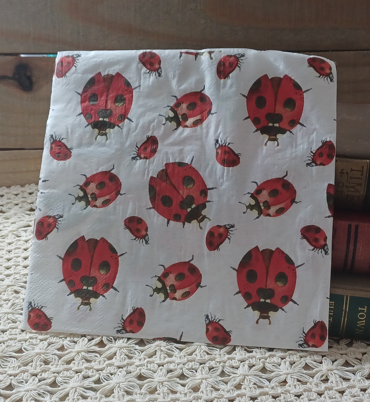 Close view of a decorative decoupage paper napkin featuring assorted red ladybugs in different sizes on a pale background.