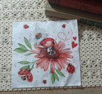 Full view of the floral side of a ladybug decorative paper napkin with a red ladybug, pink flower, white daisy, green leaves, hearts, and small garden insects.