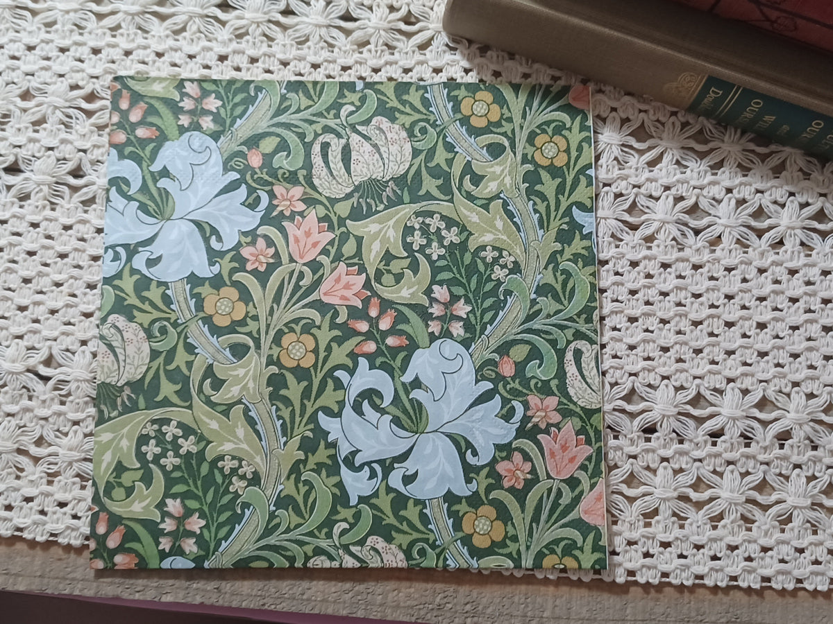 Decorative paper napkin with an ornate Arts and Crafts-inspired floral pattern featuring pale lilies, pink and gold flowers, and curling green foliage on a dark green background.