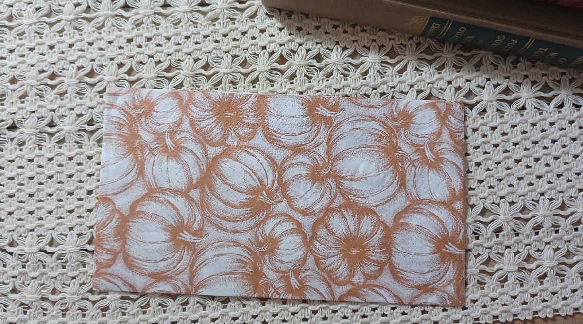 Overhead view of a rectangular decorative paper guest towel covered with hand-drawn pumpkins in warm sepia and rust tones on a white background.