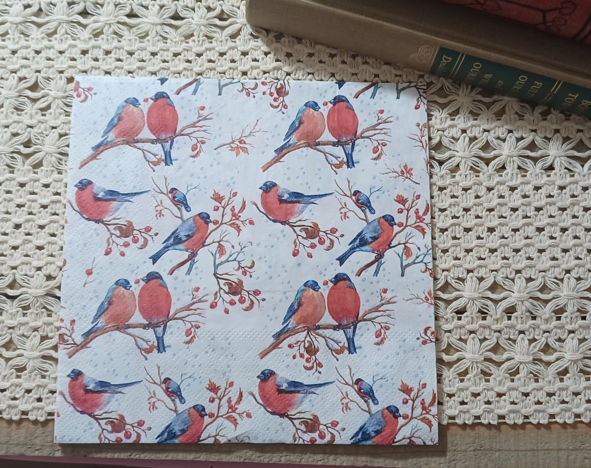 Decorative paper napkin featuring watercolor-style red-breasted birds perched on delicate branches with red berries and pale blue snow dots on a white background.