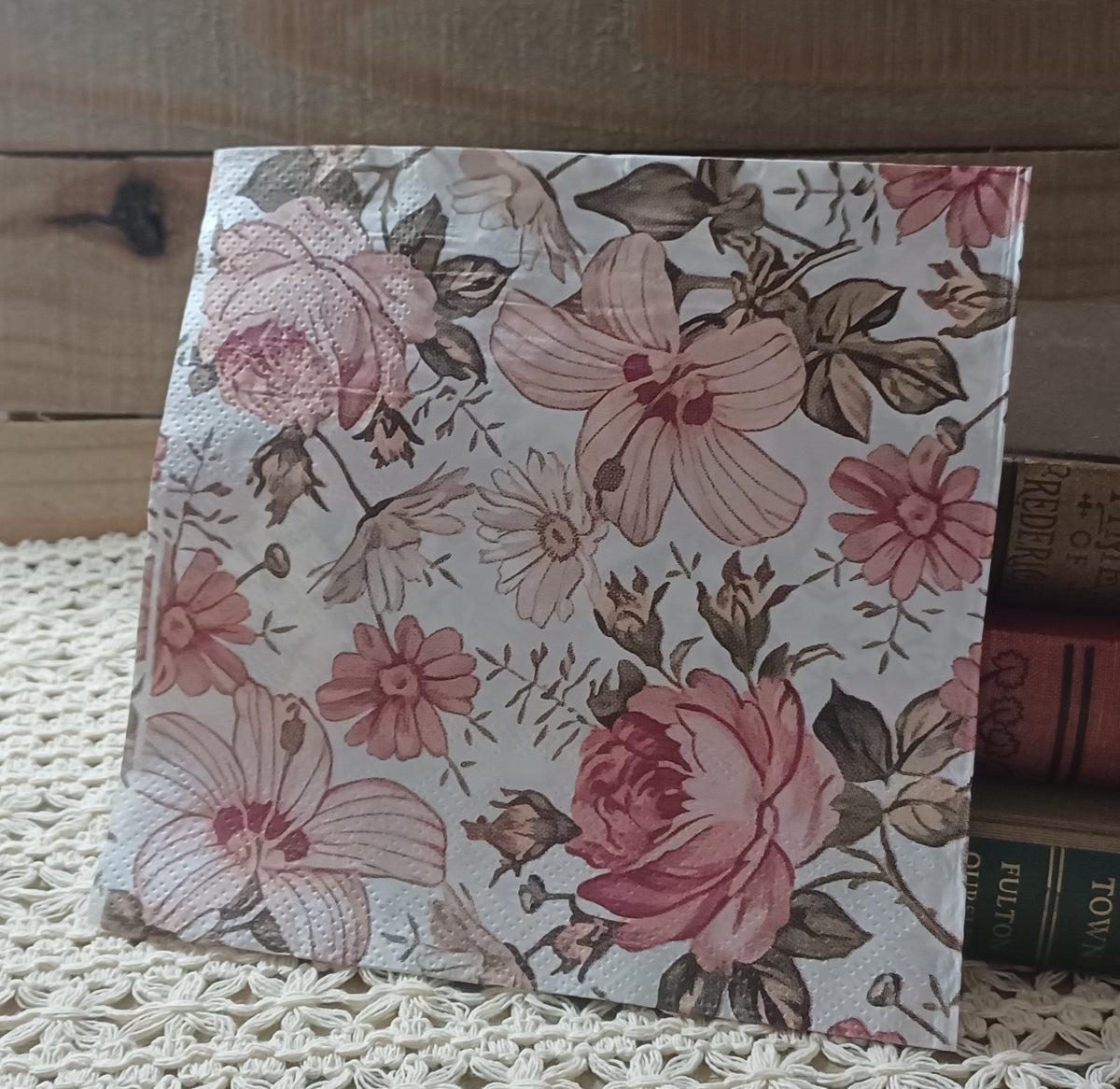 Overhead view of a single vintage-style floral decoupage napkin with dusty pink roses, blush garden flowers, delicate stems and muted taupe and brown leaves.