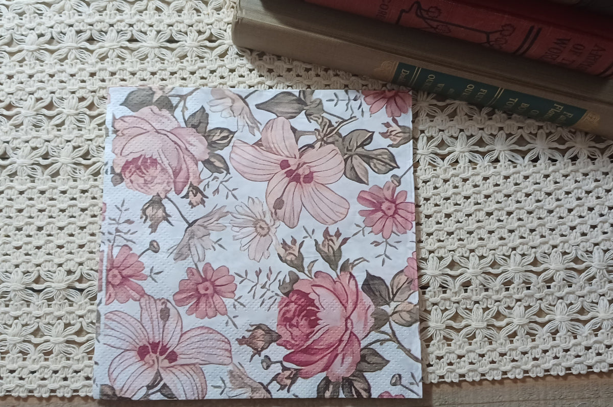 Decorative paper napkin featuring large dusty pink roses, pale open-petaled flowers, small blossoms, buds and muted brown botanical leaves on a soft cream background.