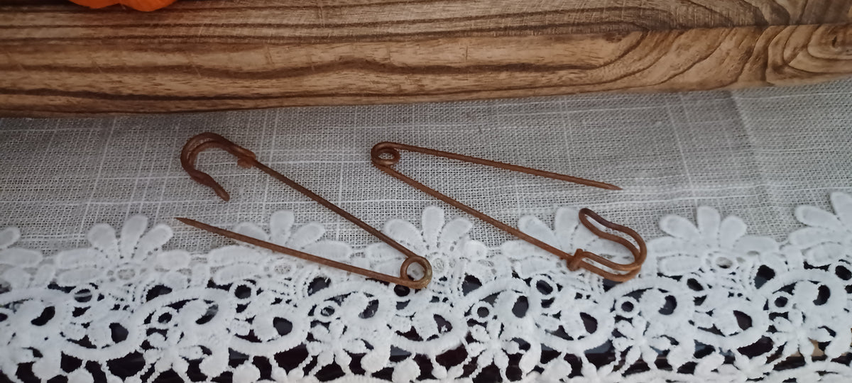 Two large industrial-style clothing pins with an uneven genuine rust finish displayed on a lace-covered surface