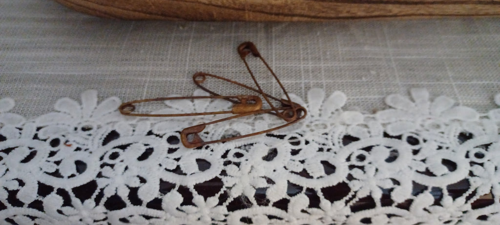 Four 2-inch metal safety pins with varied reddish-brown genuine rust finishes displayed on a lace-covered surface