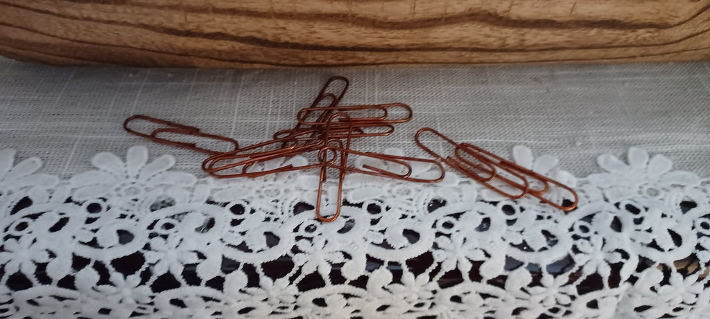 Ten 2-inch paper clips with a warm reddish-brown decorative faux-rust finish displayed on white lace