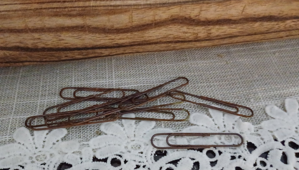 Ten 2-inch metal paper clips with varied reddish-brown genuine rust finishes displayed on a lace-covered surface
