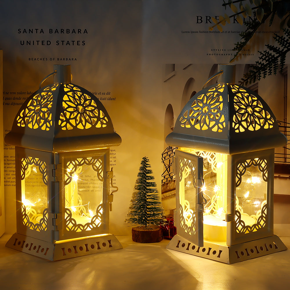 Pair of vintage-style metal lanterns with decorative cutout panels and glowing LED fairy lights, displayed among seasonal decorations.