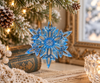 Handmade blue resin snowflake Christmas ornament hanging from a snowy evergreen branch beside vintage books and warm holiday lights.