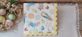 Easter bunny decorative luncheon napkin with rabbits, chicks, ducks, butterflies and pastel eggs displayed with spring flowers and Easter eggs.