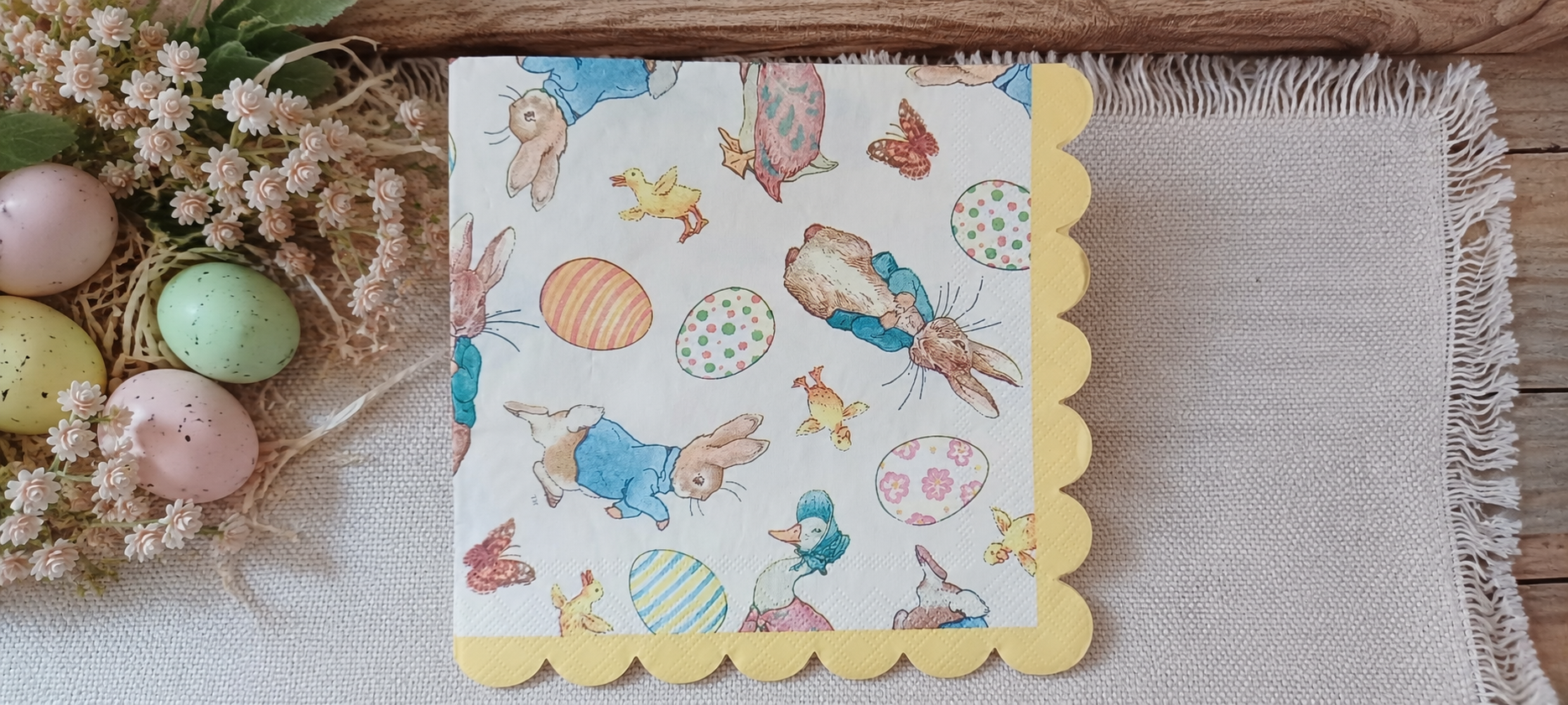 Easter bunny decorative luncheon napkin with rabbits, chicks, ducks, butterflies and pastel eggs displayed with spring flowers and Easter eggs.