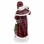 A Santa Claus figurine shown from the back, wearing a textured dark red robe with white trim, holding a small green tree and a letter, on a white background.