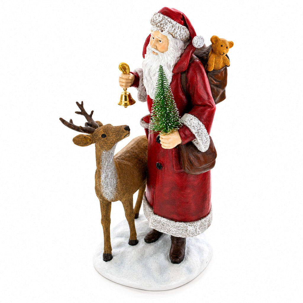 A Santa Claus figurine wearing a red coat with silver trim, holding a small Christmas tree and a gold bell, standing beside a brown reindeer on a white base. Santa has a brown teddy bear on his back, and the figurine is photographed against a plain white background.