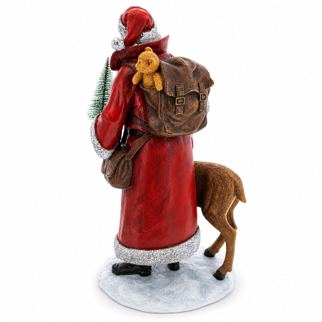 A Santa Claus figurine shown from the back, wearing a red coat with silver trim, a red hat, and carrying a brown backpack with a small yellow teddy bear. A brown reindeer stands beside him on a light blue snowy base against a white background.