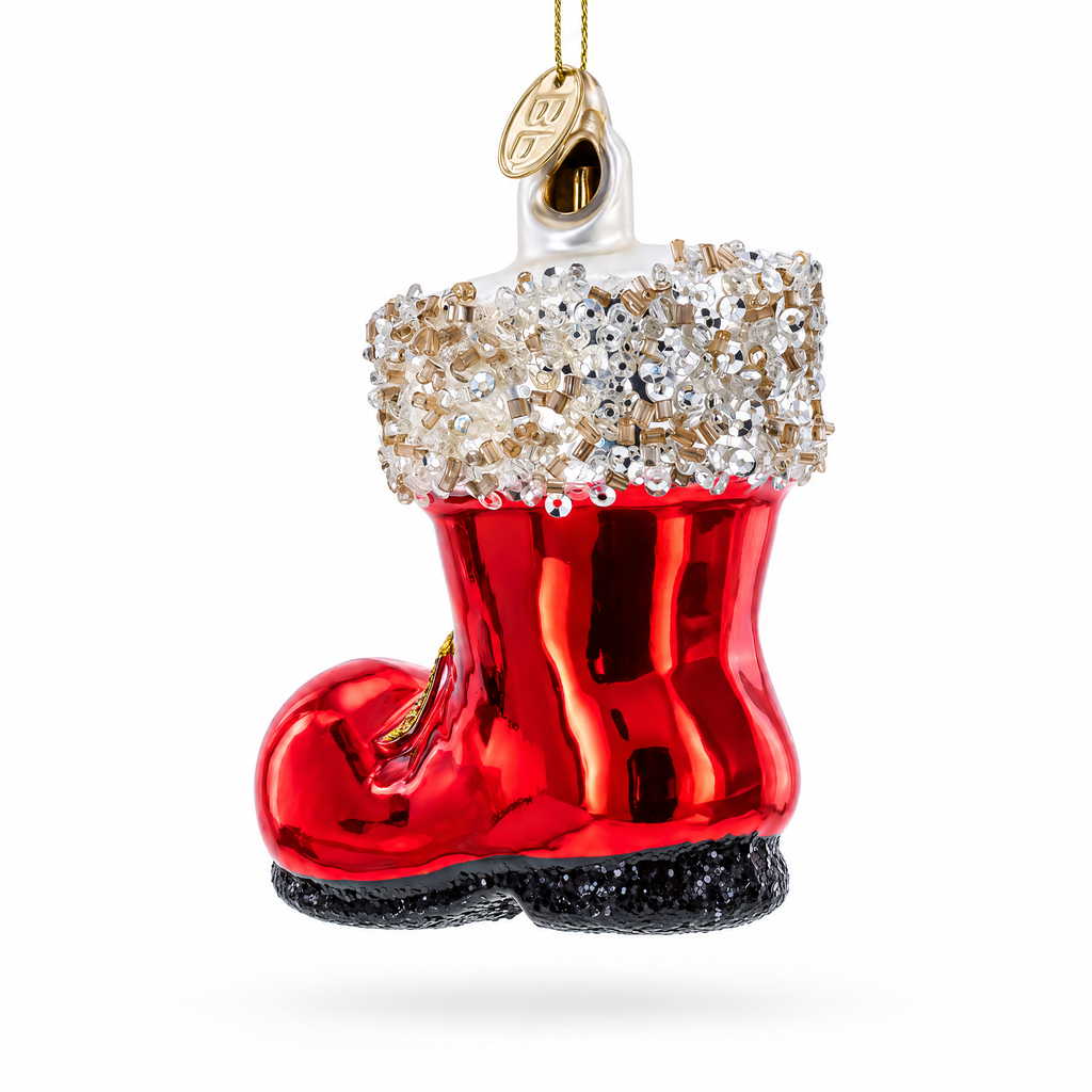 A red Christmas ornament shaped like a boot, with a white cuff covered in clear rhinestones, a black glittery sole, and a gold hanging loop at the top, shown on a plain white background.