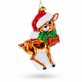 A festive Christmas ornament shaped like a deer wearing a red Santa hat with white trim, a green bow tie, and holding a red gift box, shown on a clean white background.