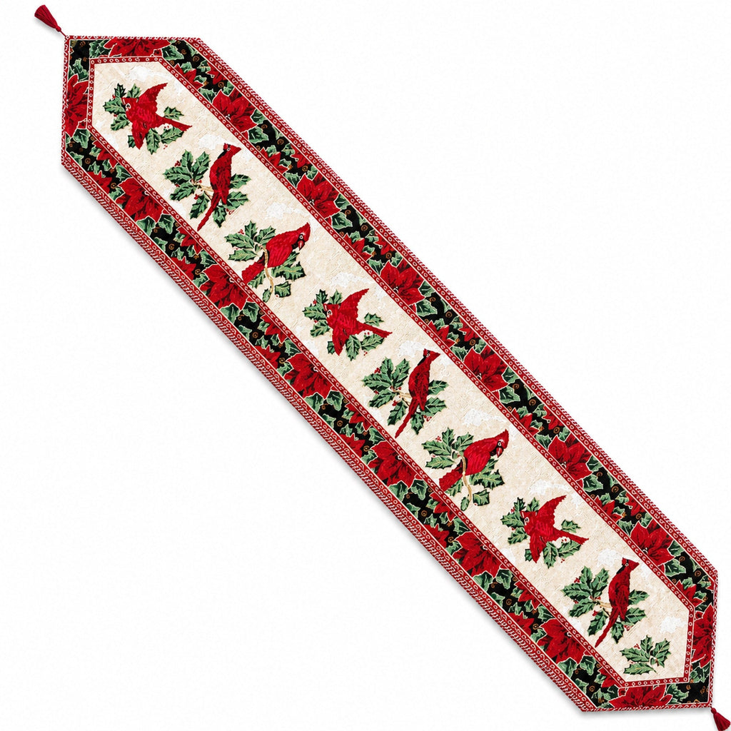 A long rectangular holiday table runner with a cream center panel featuring red cardinal birds and green holly leaves, bordered by red and green patterned fabric with tassels at the corners, shown on a white background.