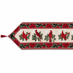 A festive Christmas table runner with a cream center panel featuring red cardinals and green holly leaves, bordered by red poinsettias and green foliage on a white background.