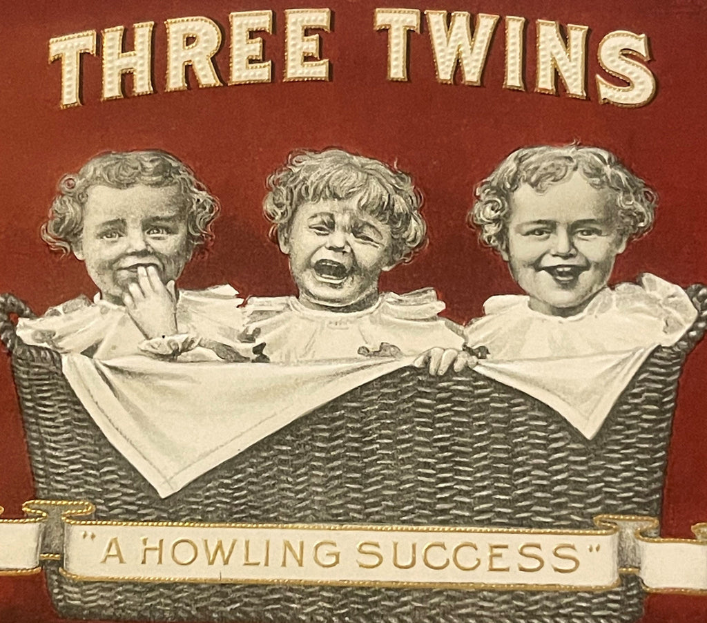 Front of antique Three Twins cigar box label featuring three babies in a wicker basket against a red background