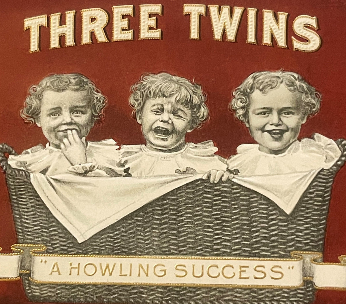 Front of antique Three Twins cigar box label featuring three babies in a wicker basket against a red background