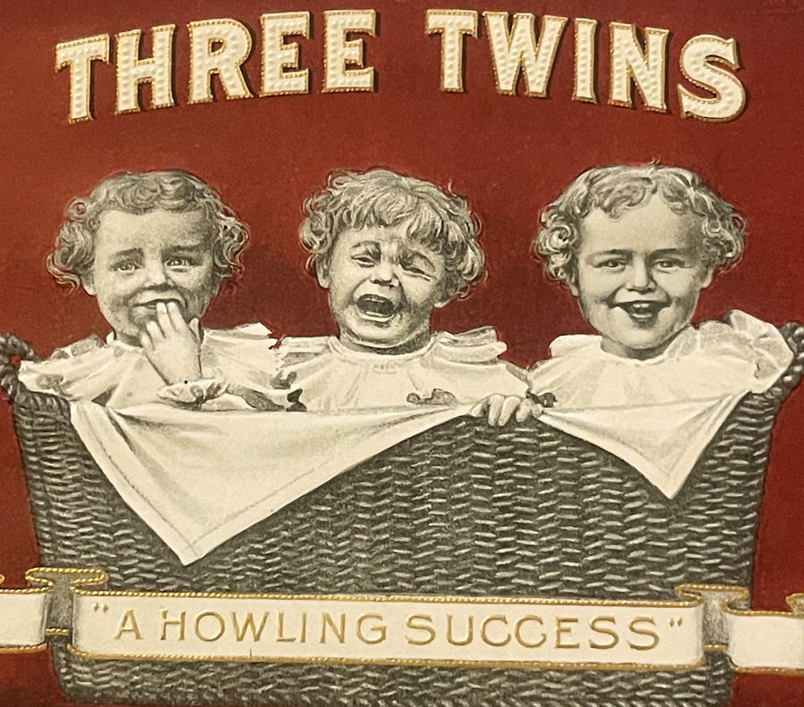 Front of antique Three Twins cigar box label featuring three babies in a wicker basket against a red background