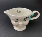White vintage Bailey’s ceramic creamer shaped like a smiling face with one eye winking, a blue bow, and a small handle.