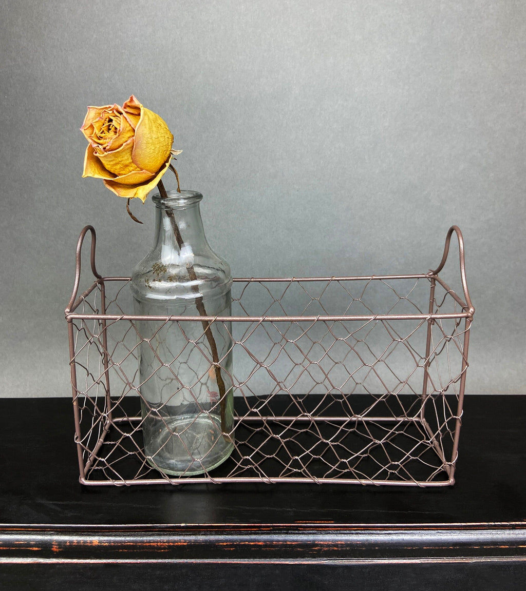 one vintage clear glass apothecary bottles in a weathered metal basket, styled with yellow flowers.