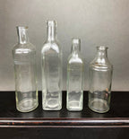 Four vintage clear glass apothecary bottles in a weathered metal basket, styled with yellow flowers.