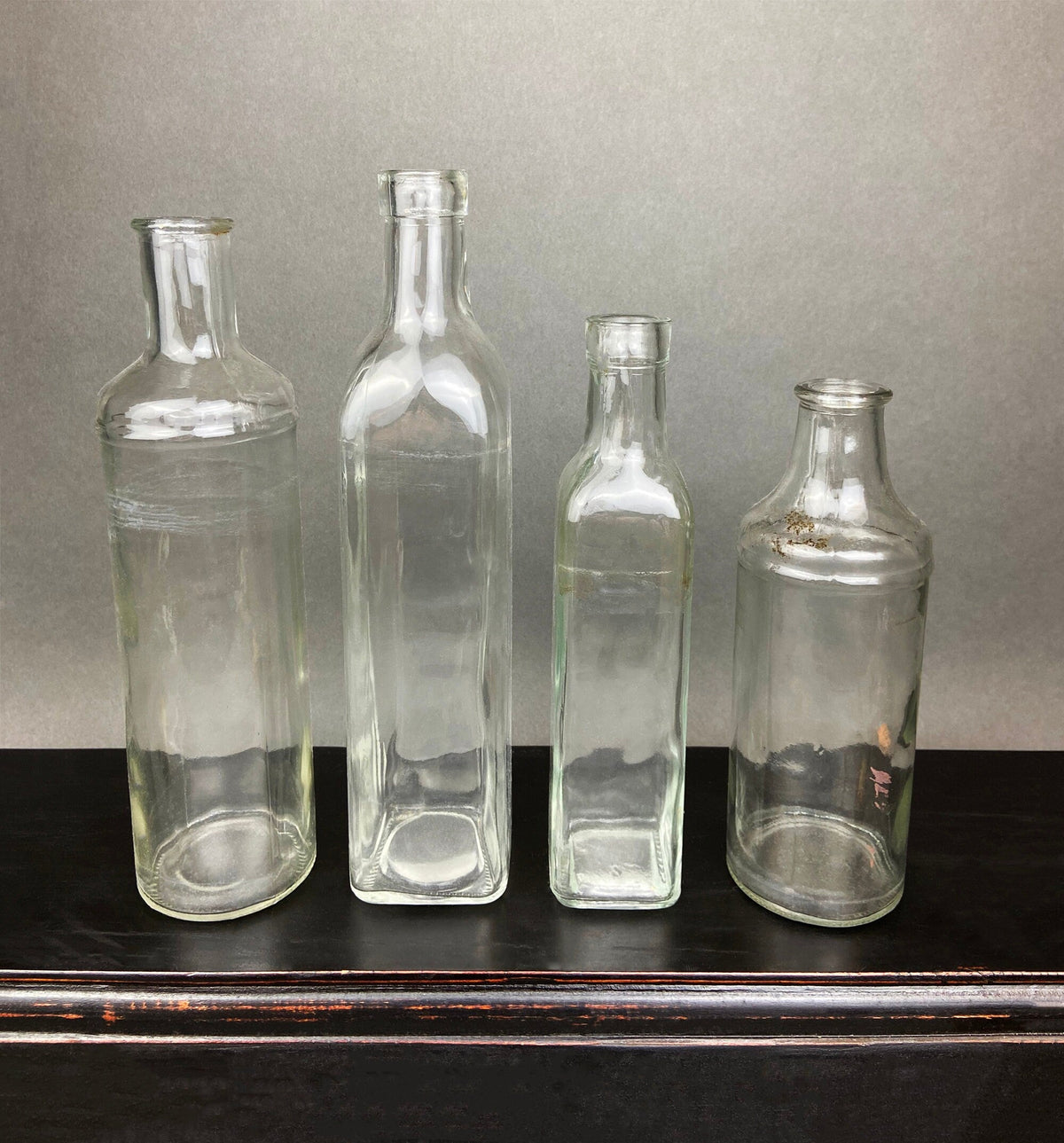 Four vintage clear glass apothecary bottles in a weathered metal basket, styled with yellow flowers.