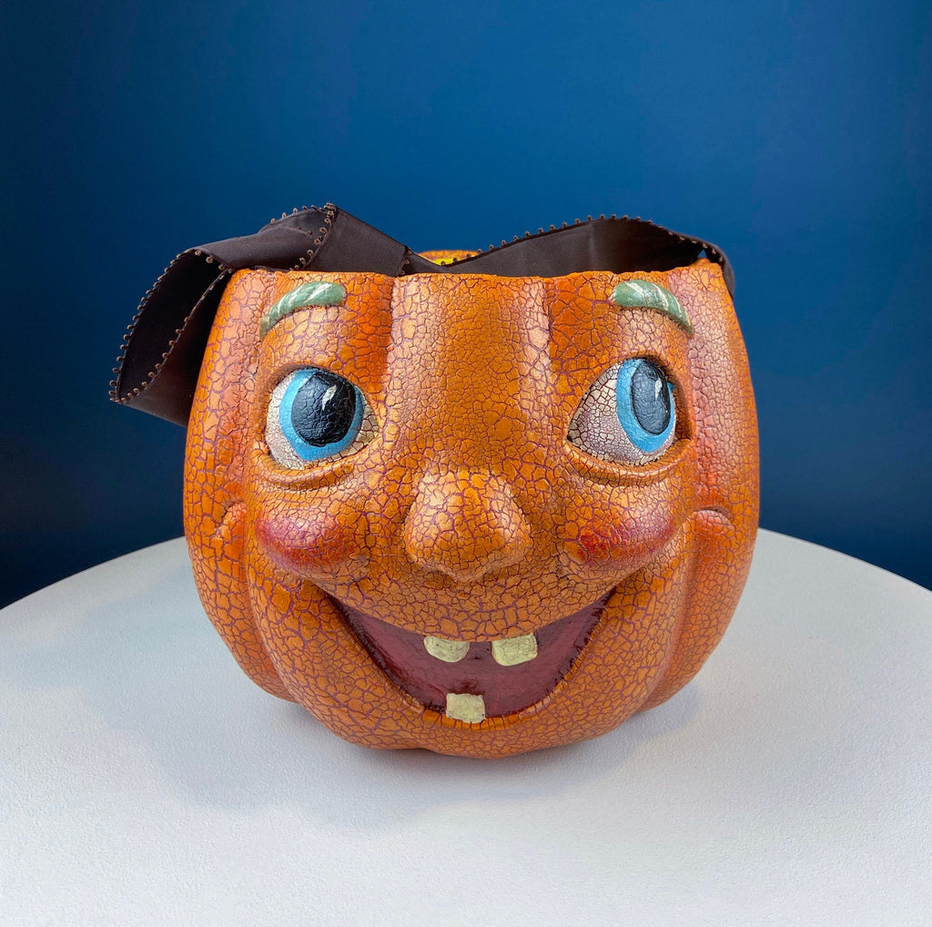 Vintage orange papier-mâché jack-o’-lantern basket with a hand-painted smiling face, blue eyes, and a crackled finish.
