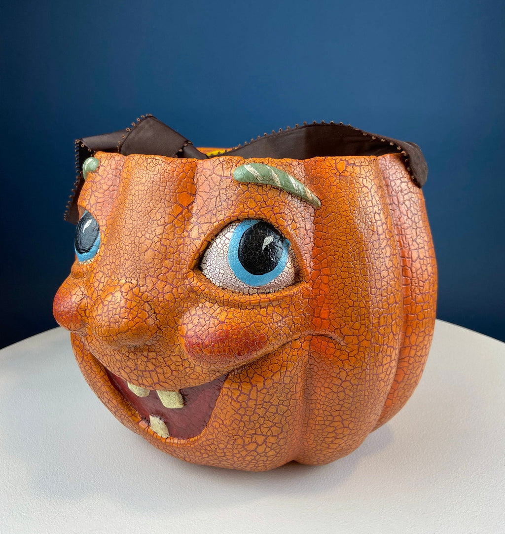Vintage orange papier-mâché jack-o’-lantern basket with a hand-painted smiling face, blue eyes, and a crackled finish.
