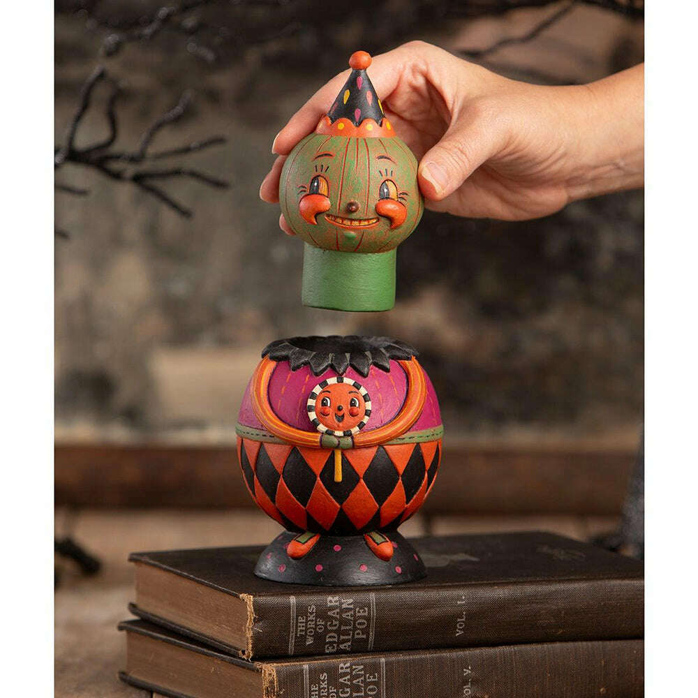 Hand lifting Jackie Green-O-Ween’s removable pumpkin head to reveal the hidden compartment inside.